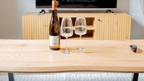 A room with a wooden table, a bottle of wine, and two glasses.