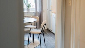 A hallway leading to a dining area with a round table and chairs, a hanging light fixture, and a window with curtains.