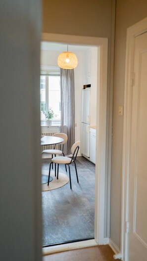 A hallway leading to a dining area with a round table and chairs, a hanging light fixture, and a window with curtains. - Clean, Quiet & Central | Sleeps 3 (Kvillebäcken)