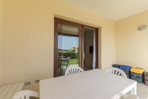 Un balcon avec une table et des chaises, une porte-fenêtre coulissante et des coffres de rangement.