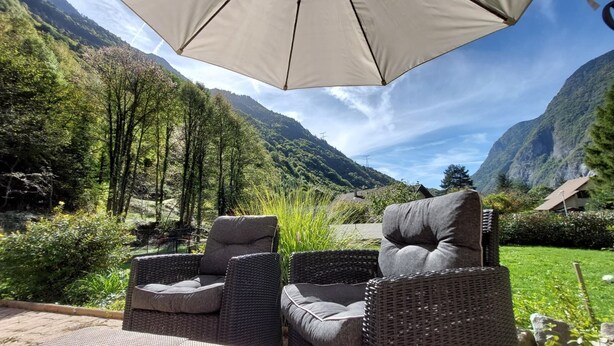 Une terrasse dotée de chaises en osier et d’un grand parasol, offrant une vue sur un paysage montagneux.