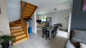 Un intérieur moderne avec un escalier en bois, un coin repas avec une table et des chaises, et une cuisine en arrière-plan.