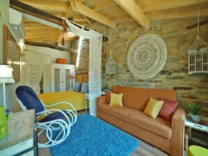 Ein gemütliches Zimmer mit Steinwand, Holzboden und einem gelben Bett, einem braunen Sofa und einem blauen Teppich.