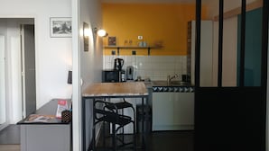 Een kleine keuken met een magnetron, waterkoker en een eettafeltje met stoelen.