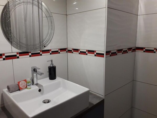 A bathroom with a white sink, a round mirror, and a red and black patterned tile border. - Les Tulipiers, centre ville, parking sécurisé (Le Mans)