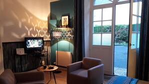 Een woonkamer met een bank, fauteuil, televisie en uitzicht door een groot raam.