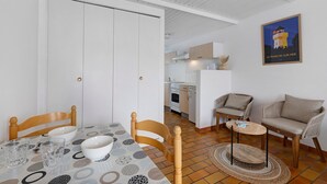 A dining area with a table set for two, a sofa, and a kitchen in the background. - Victor Studio – 200 m from the Beach (La Tranche-sur-Mer)