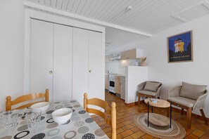 A dining area with a table set for two, a sofa, and a kitchen in the background. - Victor Studio – 200 m from the Beach (La Tranche-sur-Mer)