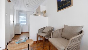 A room with wicker furniture, a round wooden table, a white door, and a window with a view. - Victor Studio – 200 m from the Beach (La Tranche-sur-Mer)