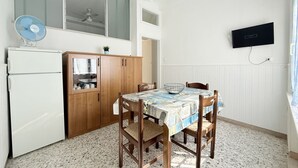 A compact kitchen with a dining table, wooden cabinets, a white refrigerator, a ceiling fan, and a mounted TV. - SE232 - Senigallia, two-bedroom apartment with private courtyard (Senigallia)