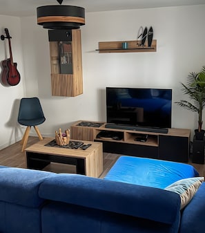 Ein modernes Wohnzimmer mit Fernseher, Holzmöbeln, einer Gitarre und einer Pflanze.