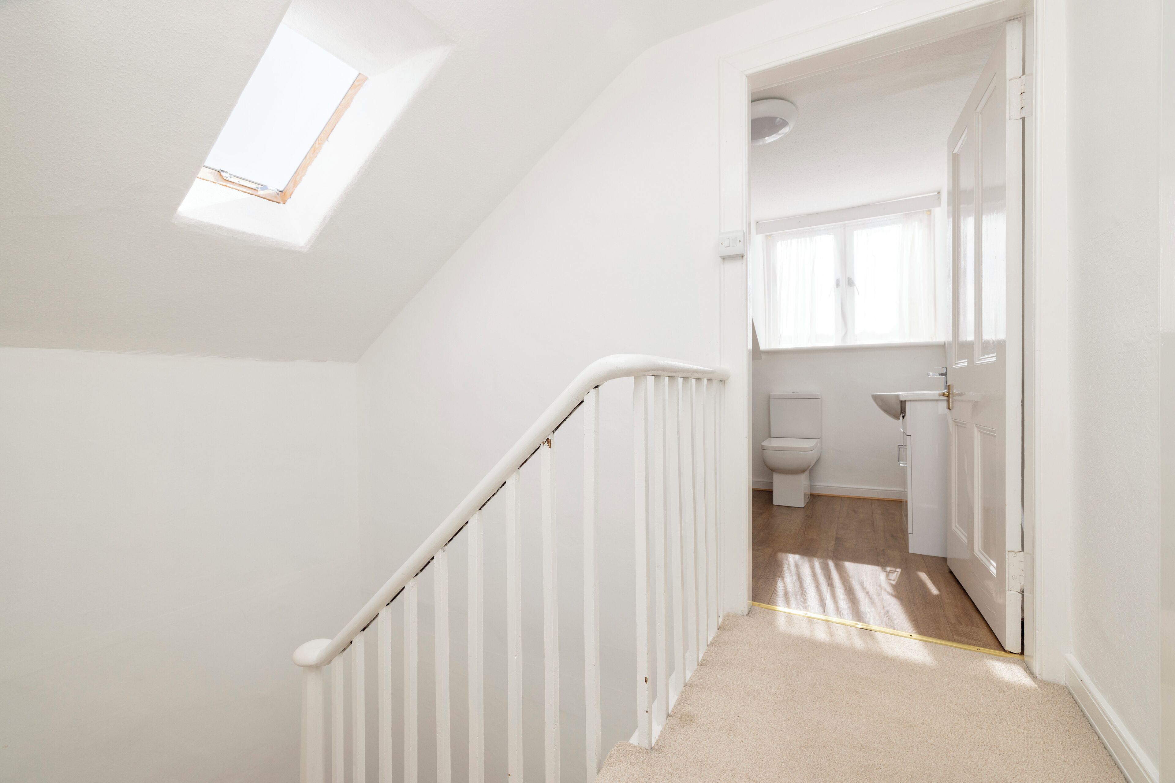 A white interior with a sloped ceiling, a white staircase, a small skylight, and a view into a bathroom.