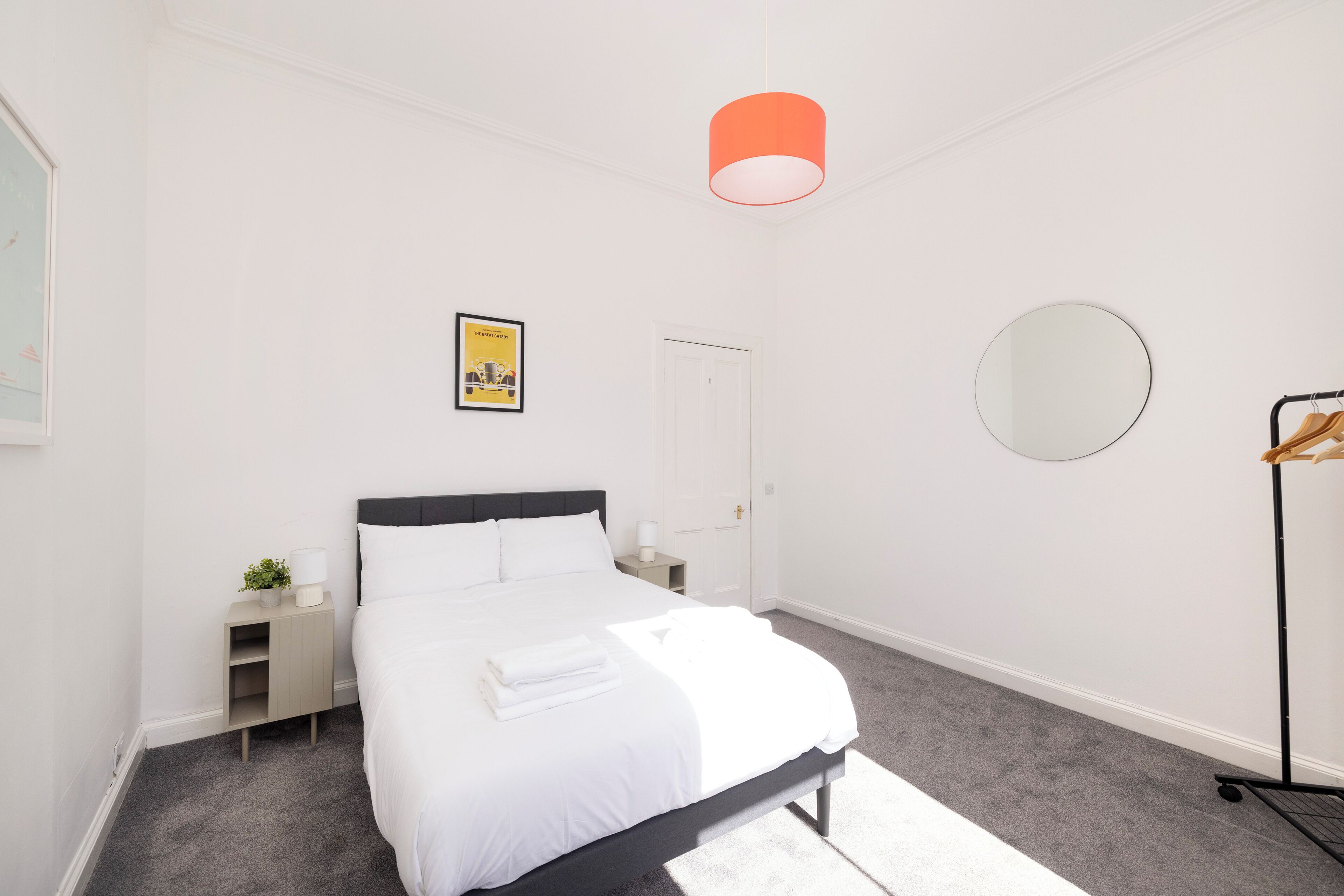A bedroom with a bed, bedside tables, a mirror, a door, and a hanging rack.