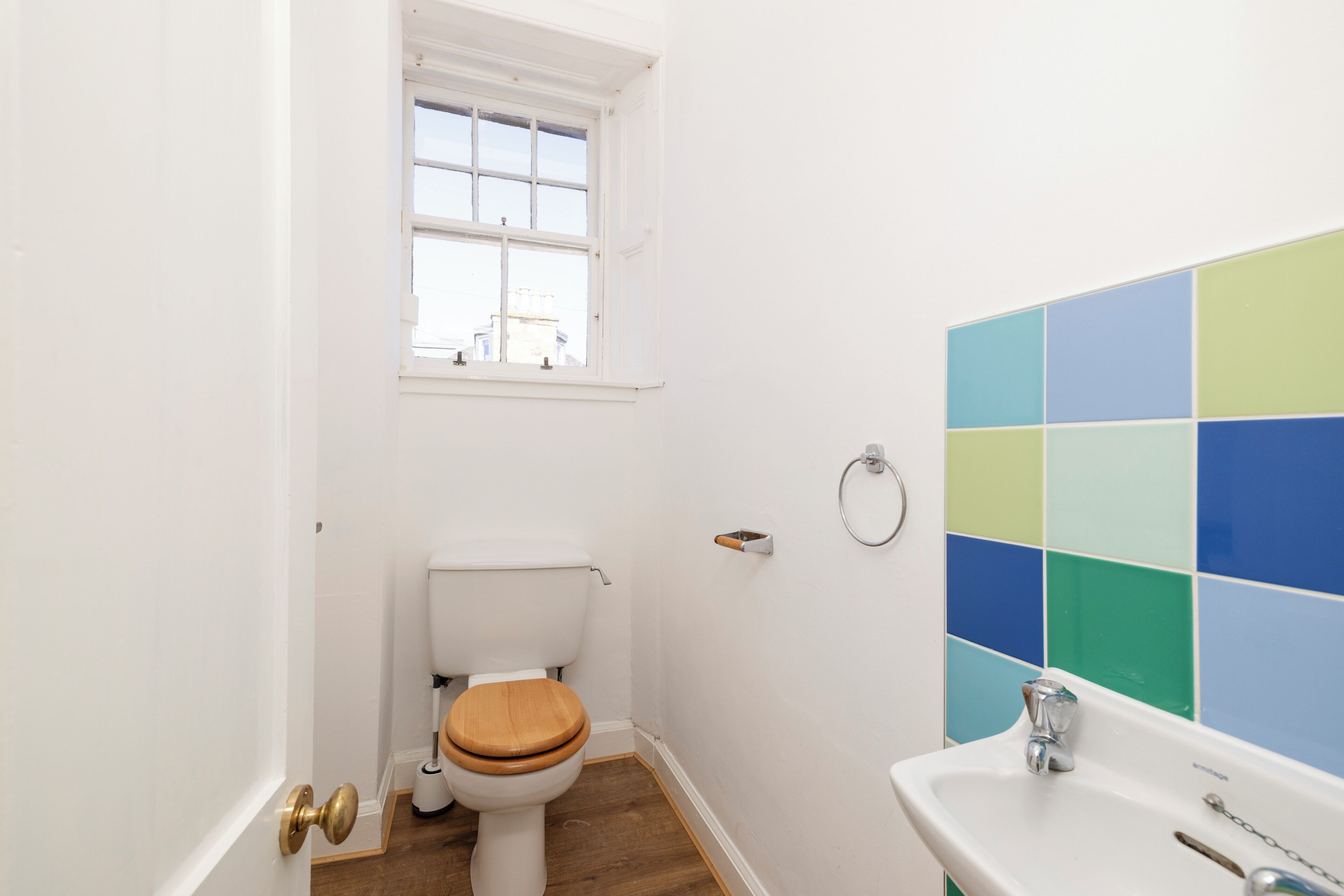 Un baño con inodoro, ventana, lavabo y pared con azulejos.