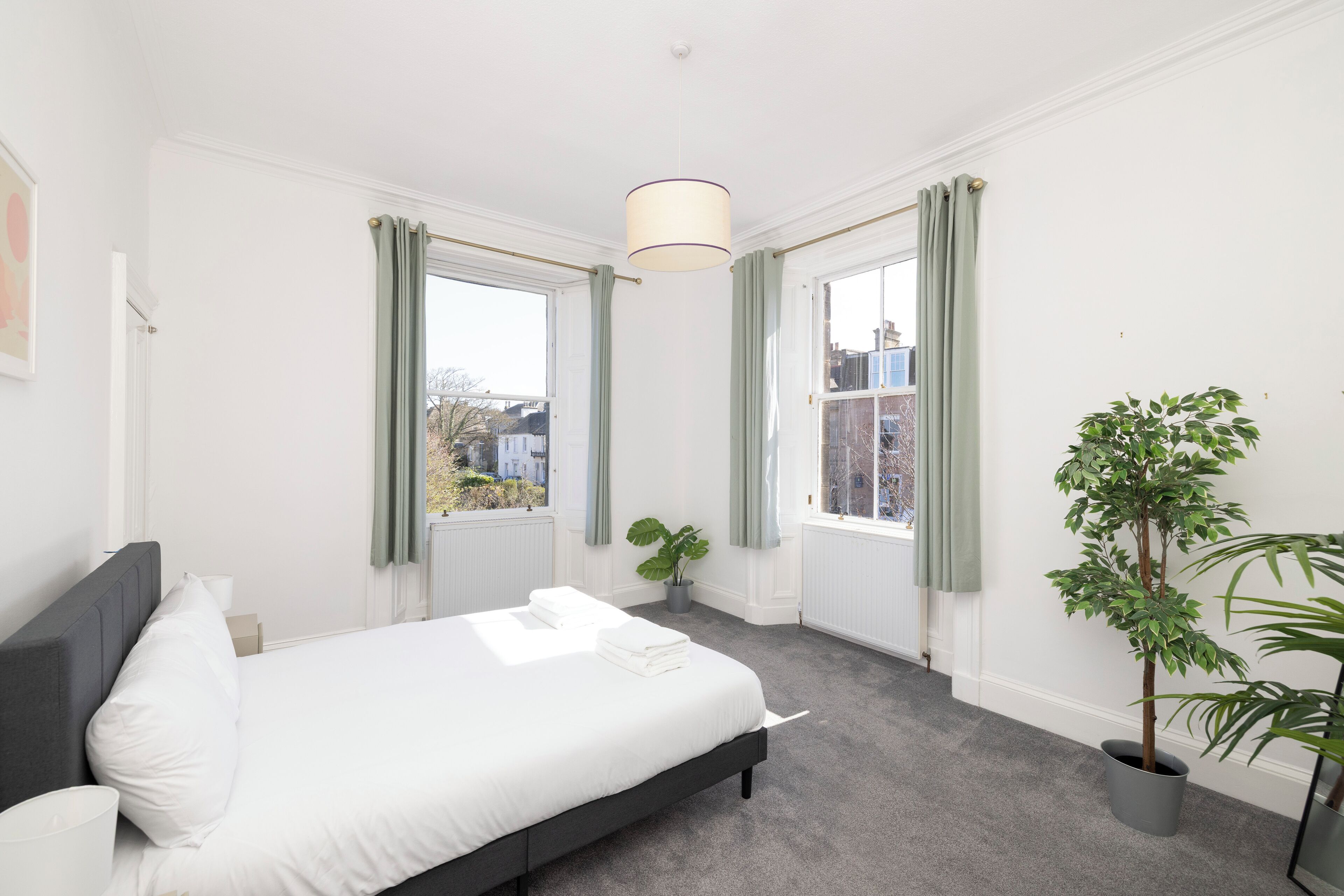 A bedroom with a bed, a window with curtains, a potted plant, and a hanging light fixture.