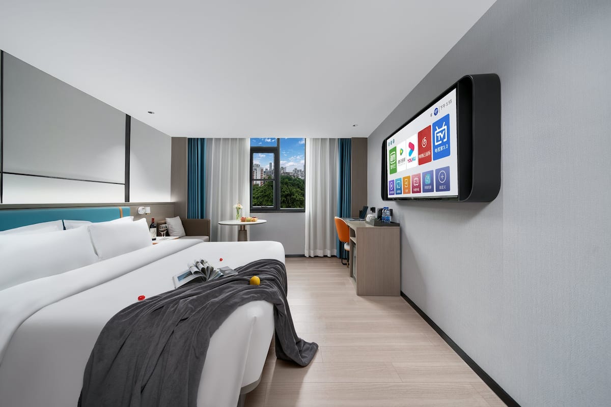 A modern hotel room with a bed, desk, and a large screen displaying hotel apps.