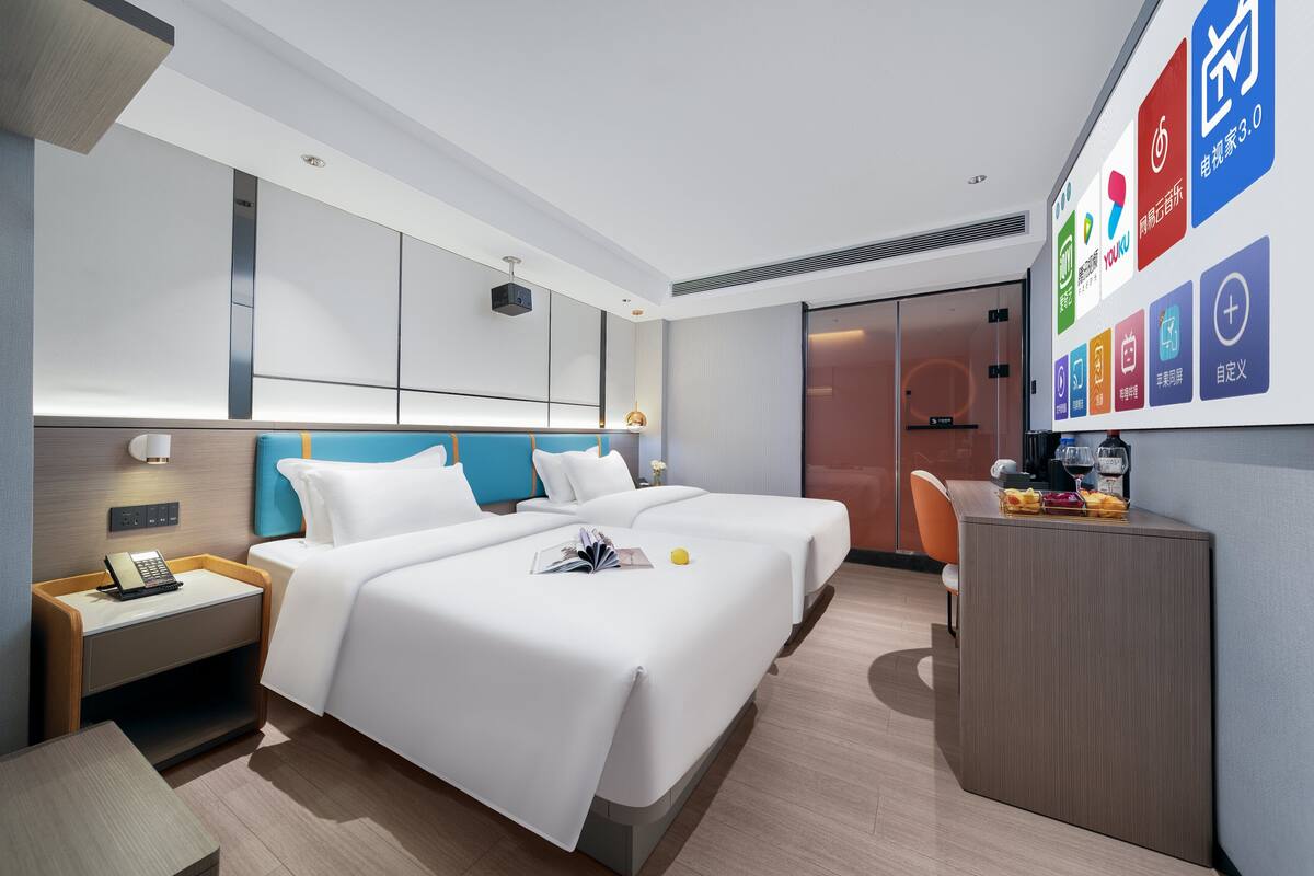 A modern hotel room with a large bed, a desk, and a TV displaying hotel amenities.