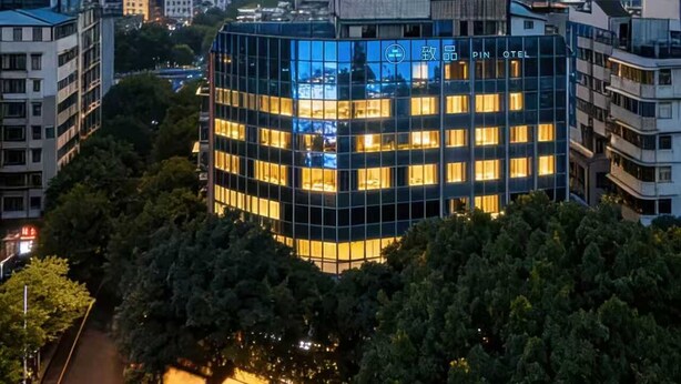 A modern hotel with a glass facade, surrounded by dense trees and a river. - PIN Hotel Guangzhou Beijing Road Pedestrian Street Gongyuanqian Metro Station Branch - Free Deliver Service to Guangzhou Baiyun International Airport & Free Deliver Service to Canton Fair Complex During Canton Fair Period (Guangzhou)
