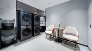A modern laundry room with stacked washers and dryers, wicker baskets, and a small table with chairs. - PIN Hotel Guangzhou Beijing Road Pedestrian Street Gongyuanqian Metro Station Branch - Free Deliver Service to Guangzhou Baiyun International Airport & Free Deliver Service to Canton Fair Complex During Canton Fair Period (Guangzhou)