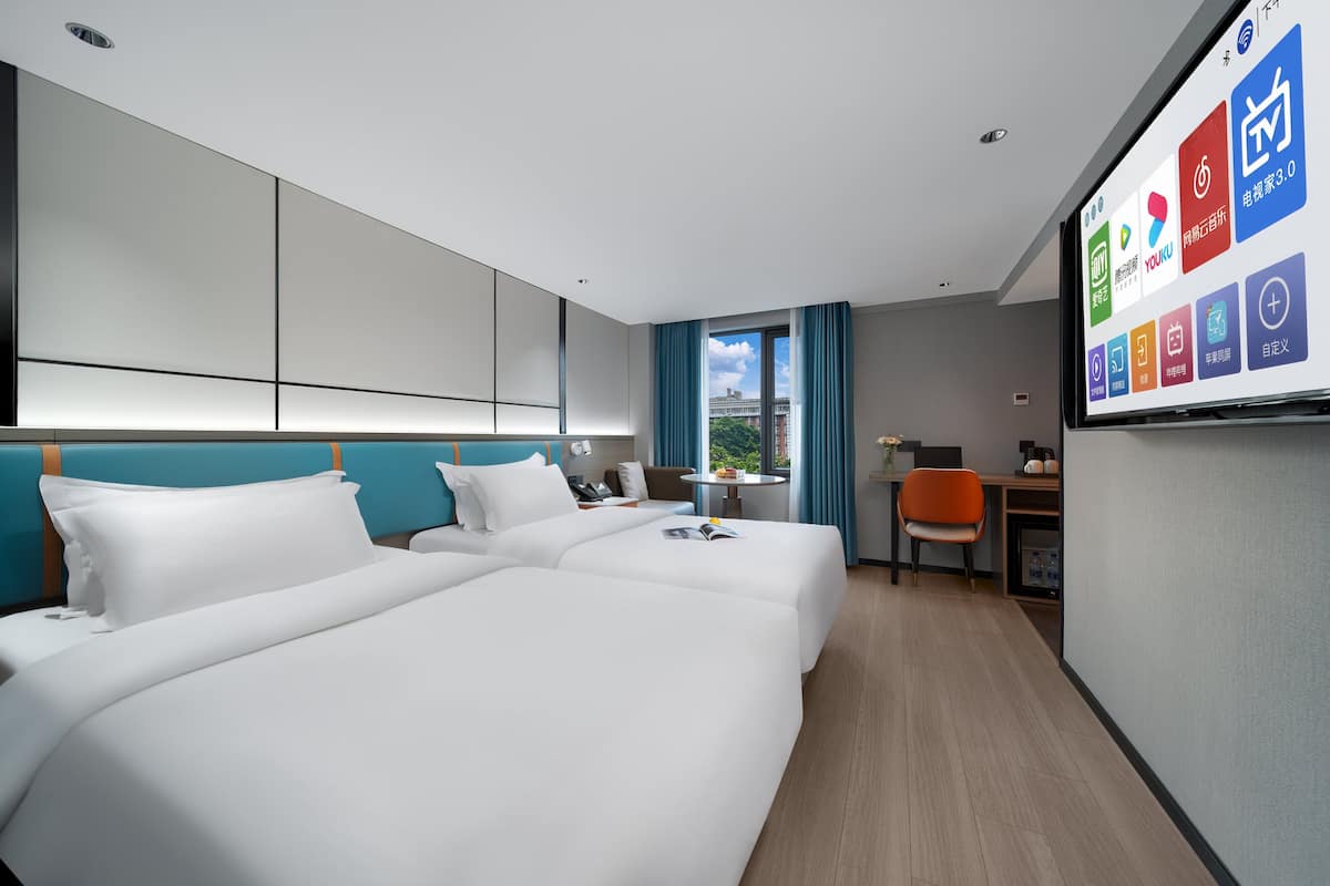 A hotel room with two beds, a desk, a chair, and a large window.
