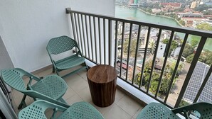 Un balcon avec quatre chaises en plastique vertes, un tabouret en bois et une vue sur un paysage urbain avec une tour.