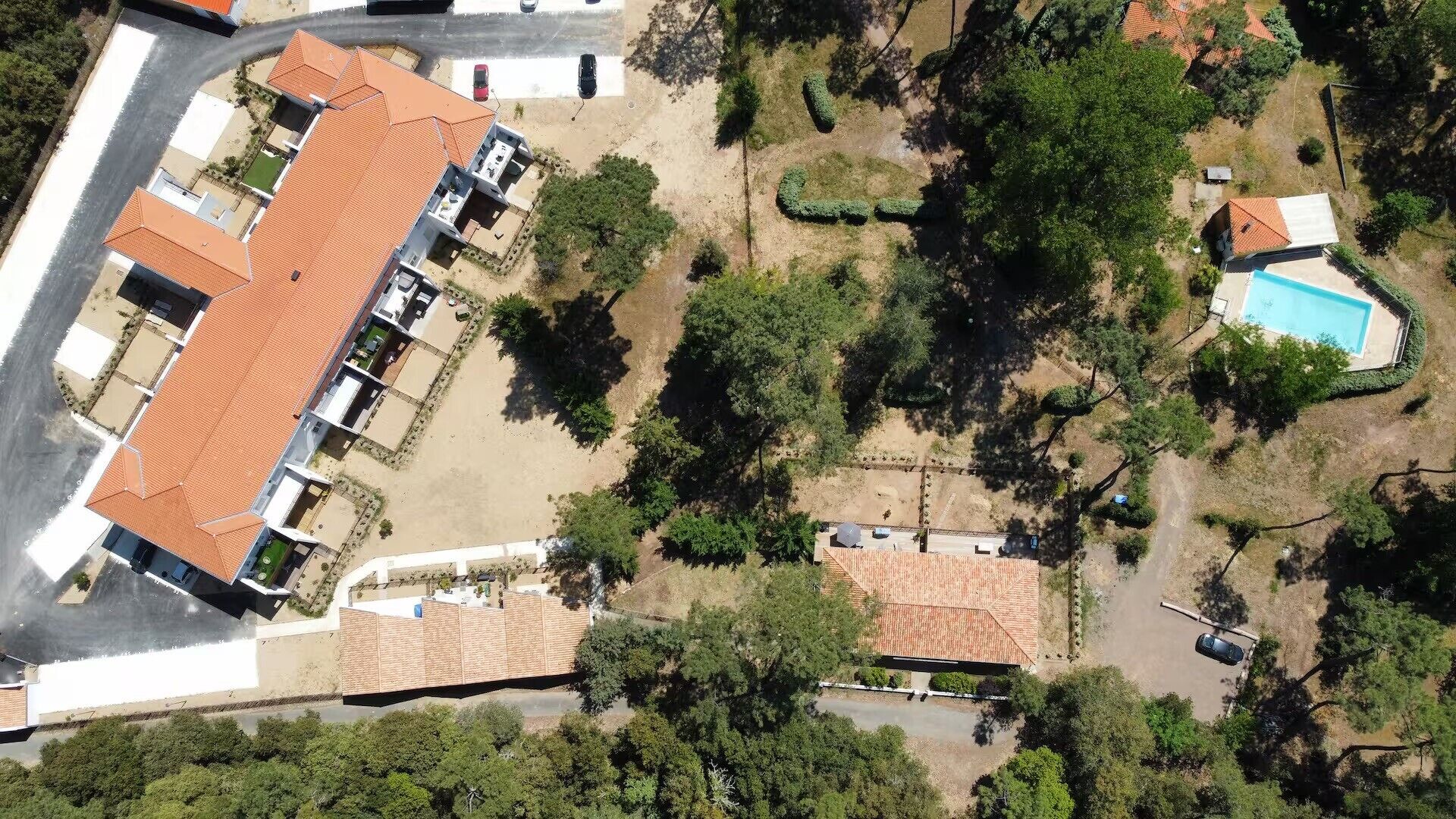 An aerial view of a residential area with a large building with a red roof, surrounded by trees and a swimming pool.