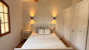 Quarto com cama, mesas de cabeceira, guarda-roupa e uma janela.