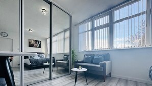 A modern living room with a glass partition, a sofa, a coffee table, and a bed with a view through the window. - Home Studio  Free Parking Prime Location (Slough)