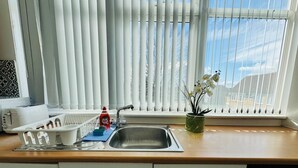 A kitchen with a sink, a dish rack, a dish soap bottle, a potted orchid, and a window with blinds. - Home Studio  Free Parking Prime Location (Slough)