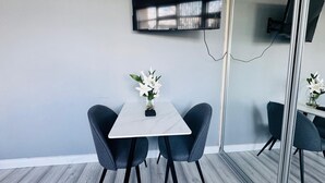 A modern room with a white table, two chairs, a vase with white flowers, and a flat-screen TV mounted on the wall. - Home Studio  Free Parking Prime Location (Slough)