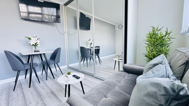 A modern living room with a grey sofa, two armchairs, a small coffee table, and a TV mounted on the wall. - Home Studio  Free Parking Prime Location (Slough)