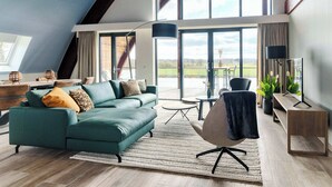 A spacious living area with a large window, a sofa, a chair, a coffee table, and a TV stand. - Private Wellness Haven by the Vecht (Dalfsen)