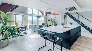 A modern kitchen with a central island, a dining area with a round table, and a staircase leading to an upper level. - Private Wellness Haven by the Vecht (Dalfsen)