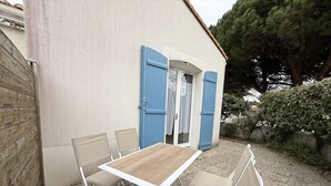 Un patio al aire libre con una mesa, sillas, una puerta azul y suelo de grava.