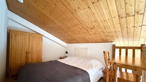 Un dormitorio con techo de madera, una cama, una mesita de noche, un escritorio y una silla.