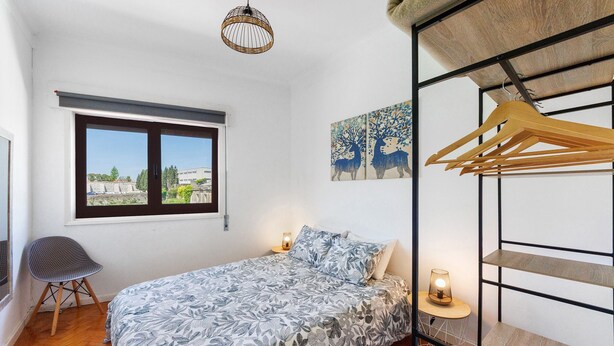 Une chambre à coucher comprenant un lit, une chaise, une fenêtre, un luminaire suspendu et un mur décoré d’œuvres d’art.