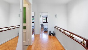 Un couloir doté d’un plancher en bois, de murs blancs et d’un plafond en verre. Deux portes se trouvent sur le côté gauche, dont une est ouverte et donne sur une pièce dont le mur est vert.