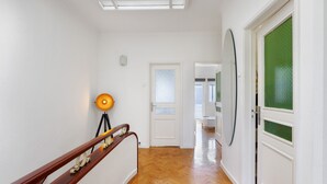 Un couloir doté d’un plancher en bois, de murs blancs, d’une porte avec un panneau en verre dépoli et d’une lampe posée sur un trépied.