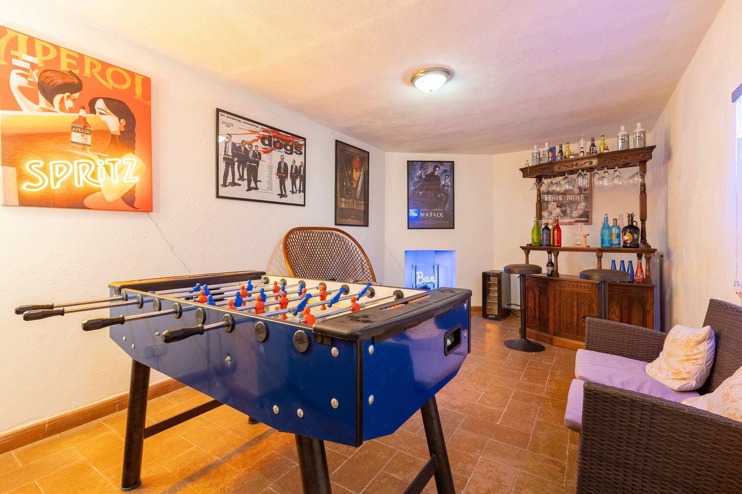 Una habitación con mesa de fútbol de mesa, zona de bar con botellas y carteles de películas enmarcados en la pared.