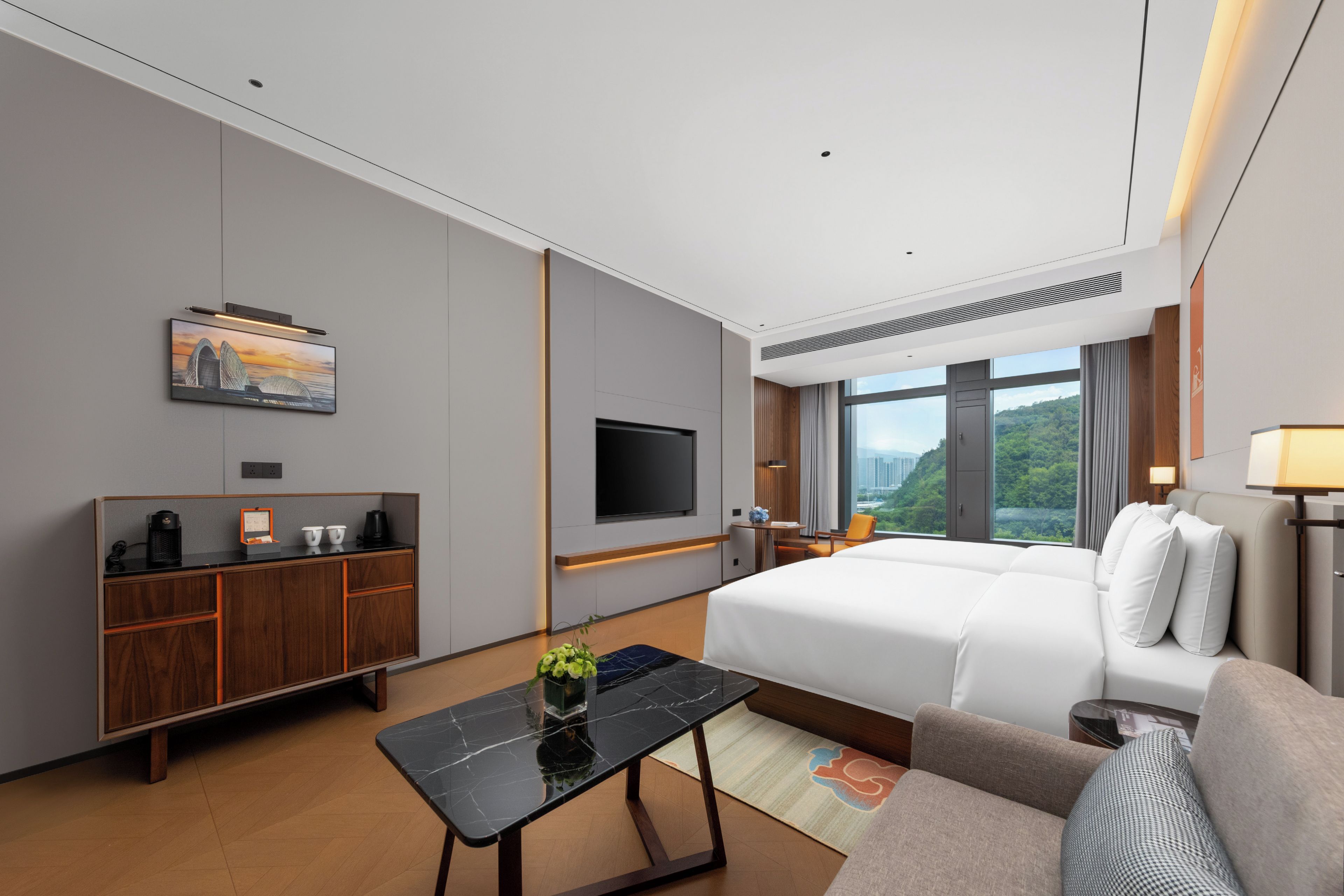 A modern hotel room with a bed, a desk, a television, and a large window offering a city view.