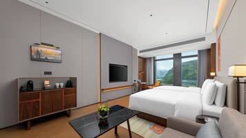 A modern hotel room with a bed, a desk, a television, and a large window offering a city view.