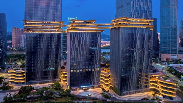 Un moderno complejo de edificios de gran altura con varios rascacielos, que presenta un atrium central con balcones curvos y vista al río.