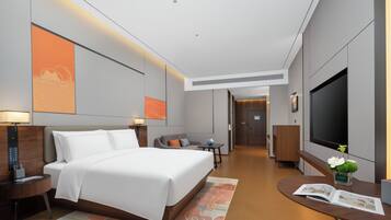 Une chambre d’hôtel moderne, dotée d’un grand lit, d’un bureau, d’une chaise, d’une télévision et d’une petite table sur laquelle est posé un magazine.