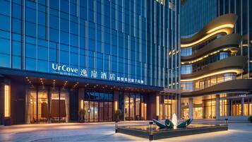 A modern hotel building with a glass facade, a well-lit entrance, and a landscaped area with a water feature.