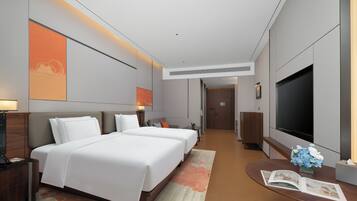 A hotel room with two beds, a flat-screen TV, a desk with a magazine, and a large window.