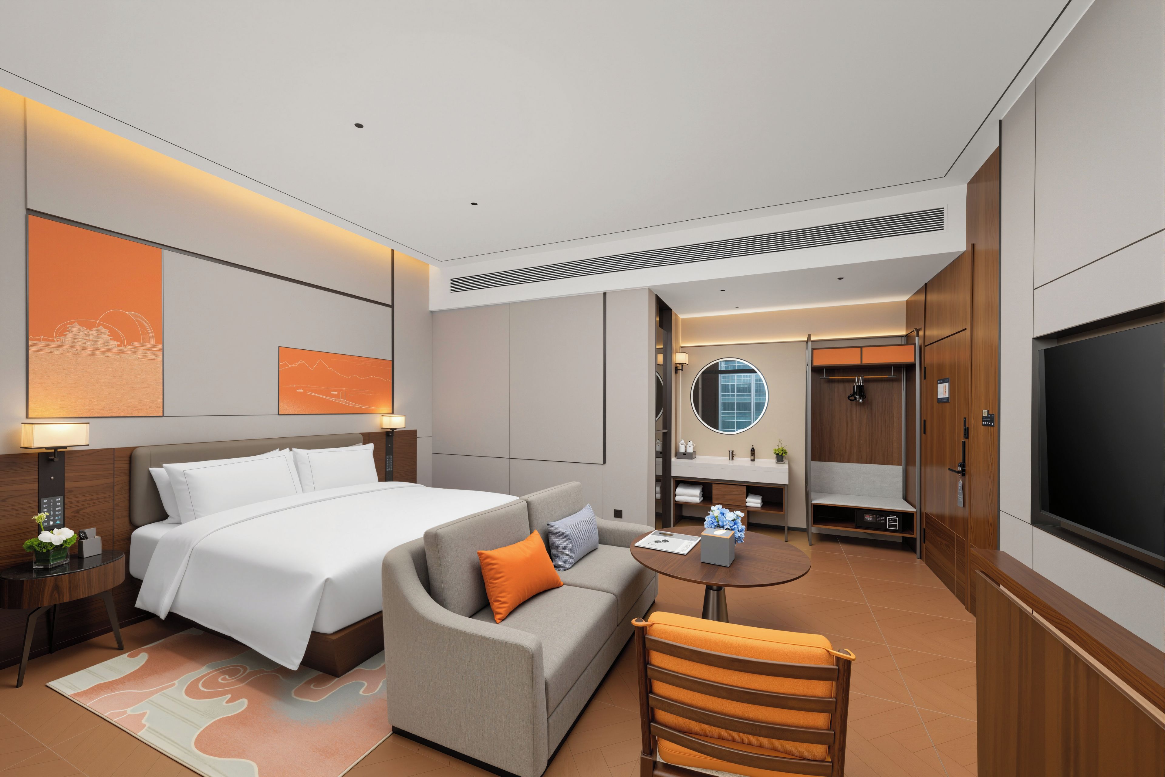A hotel room with a bed, a sofa, a small table, a TV, and a bathroom visible through an open door.