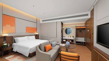 A hotel room with a bed, a sofa, a small table, a TV, and a bathroom visible through an open door.
