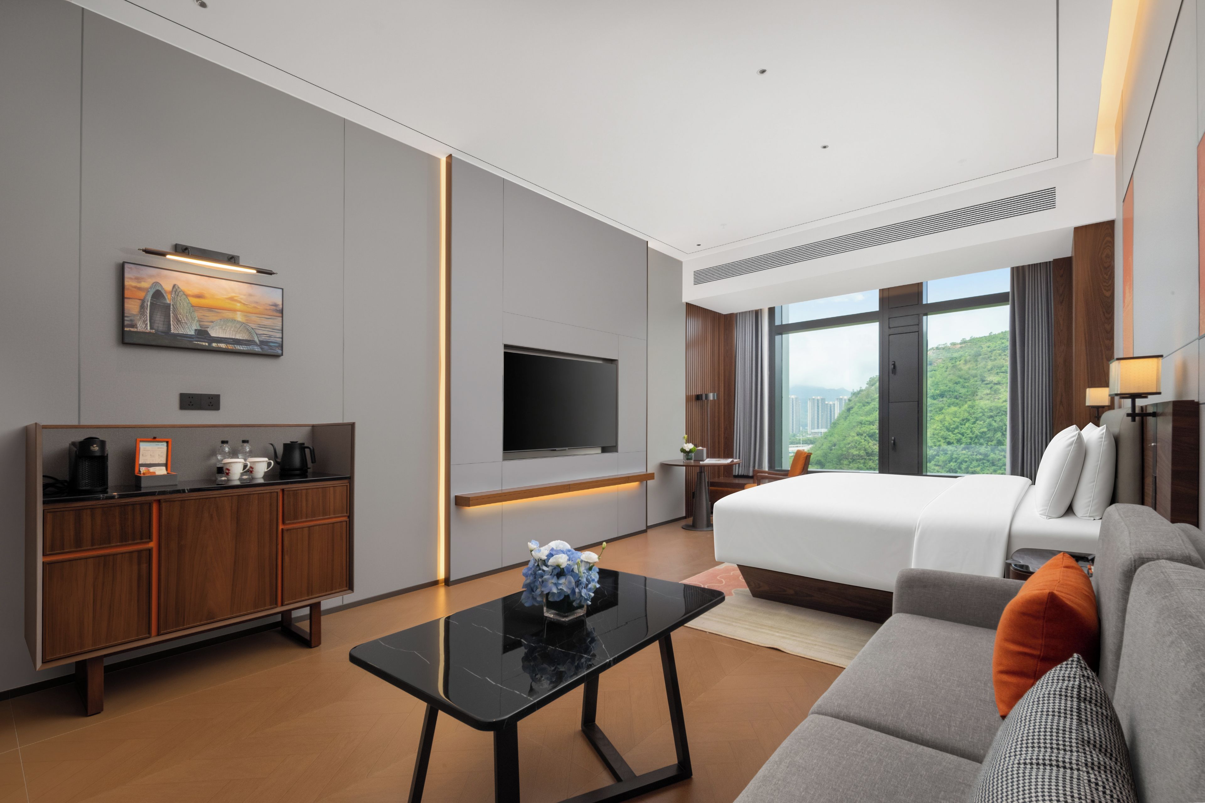 A modern hotel room with a bed, sofa, TV, and a desk with a coffee maker.