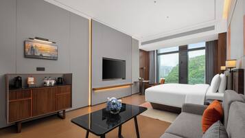 A modern hotel room with a bed, sofa, TV, and a desk with a coffee maker.