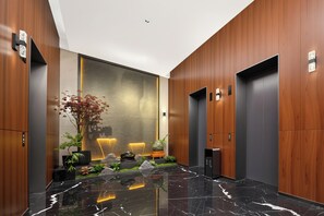 A modern elevator lobby with wooden paneling, a marble floor, and a plant arrangement.